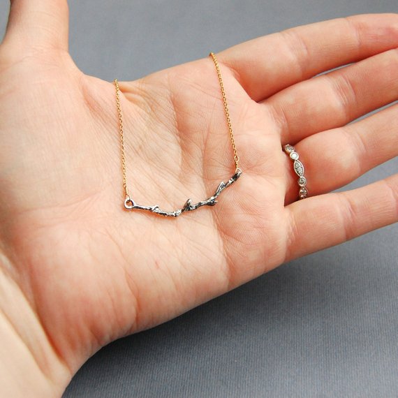 A lightly oxidized branch charm is suspended in the middle of a 14k gold filled chain, displayed on a palm for size reference. The branch is approximately 2" across.