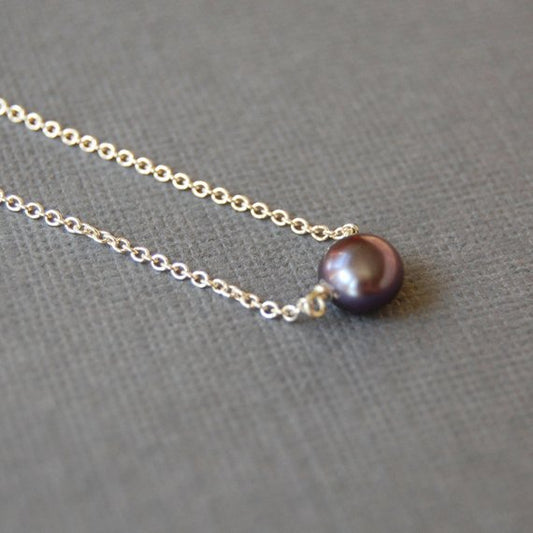 Closeup of a single round grey pearl linked on a delicate sterling silver chain. The pearl is drilled off center, so it hangs more like a pendant than a bead.