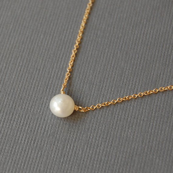 Closeup of a white pearl on a grey background from the opposite angle. The pearl is drilled off-center, so it hangs more like a pendant. The pearl is on a delicate 14k gold filled chain.